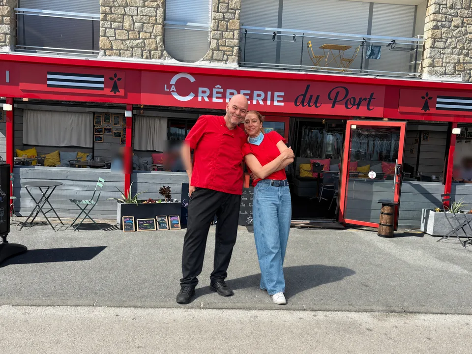 Arnault et Liliana, qui tiennent la maison, devant la devanture rouge de La Crêperie du Port à Saint-Cast-le-Guildo.